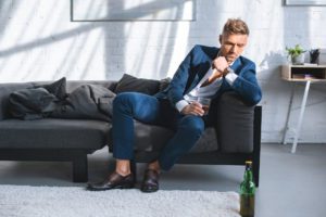 Pensive Businessman Sitting on Sofa and Holding Glass of Alcohol