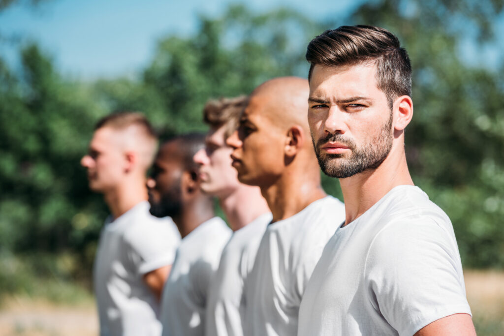 A group of men standing in line looking forward, while one man stares directly into the camera, representing the isolation and struggles in men's mental health.