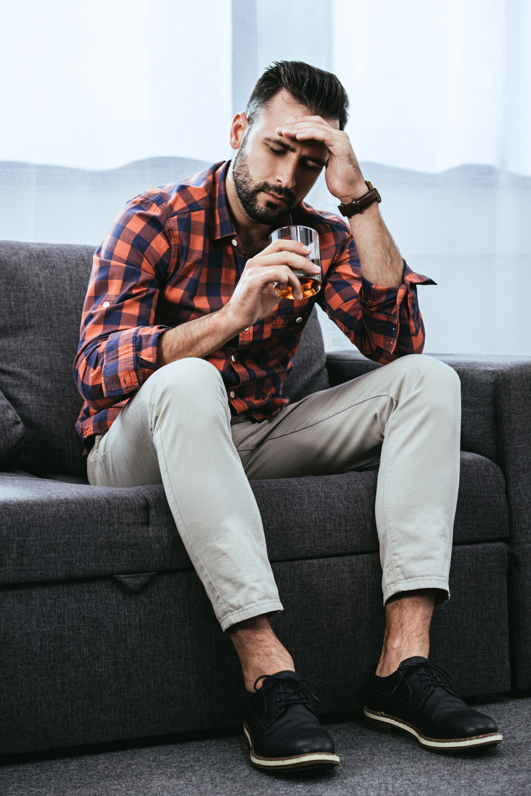 A successful, attractive man holding a glass of whiskey, looking depressed, symbolizing the struggle with high-functioning addiction in men.